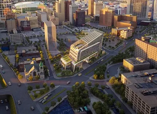 Aerial view of a modern, multi-story building with green rooftops and curved architecture, surrounded by city streets and other urban buildings.