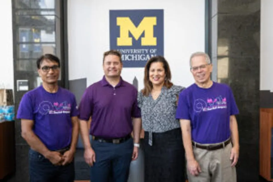 The Ally Financial team in purple shirts in front of a University of Michigan logo